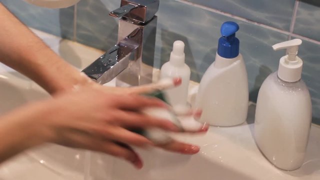 woman washing her hands using blue sponge in blue and white bathroom interior with white soap and sanitizer bottles on a sink