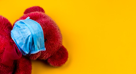 Fototapeta na wymiar Lonely Red Teddy bear in a protective medical mask on a yellow background with respiratory masks. Coronavirus covid-19 prevention concept.