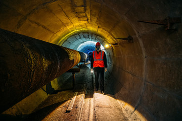 Tunnel worker examines pipeline in underground tunnel