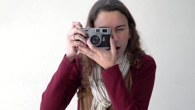 Beautiful young woman wearing scarf and long hair holding a camera, looking and taking a picture on white background. Concept of leisure, art, lifestyle, youth, happiness and photography. 4K