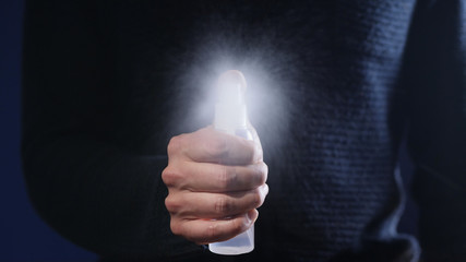 A man holding a bottle in his hand sprays a disinfectant directing the flow into the camera, closeup