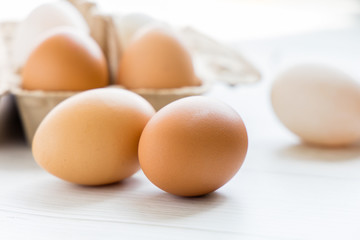 Brown and white organic chicken eggs in a brown paper box placed on a white wooden table. Eggs provide protein, suitable for health lovers.