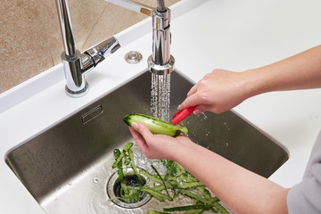 Cropped view of female hands peeling cucumber over Food waste disposer machine in sink in modern...
