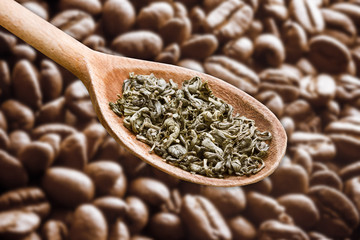 Green tea is healthy alternative for coffee. Pile of dry leaves pile. Wooden spoon of green tea isolated over coffee seeds. Proven benefits of antioxidant tea over coffee beans.