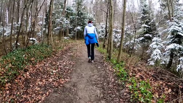 Slow motion of a young woman walking uphill, from behind, in a forest on muddy surface while snowing