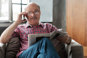 Senior man in living room reading newspaper talking on phone with his children.