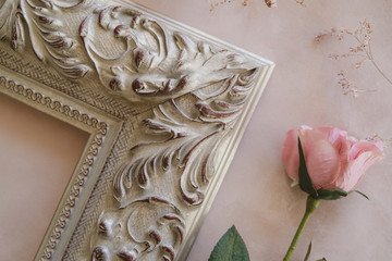 Corner of ornamental wooden empty picture frame and rose on pastel canvas backdrop.