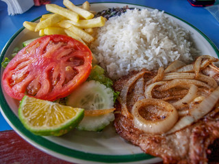 Costa rican meat dish: bistek with onions, rice, french fries, tomato, cucumber and lemon slice