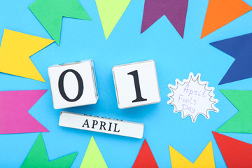 Text April Fool's Day with wooden calendar and paper flags on blue background