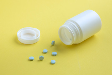 Medicamento destapado con pastillas fuera sobre un fondo amarillo