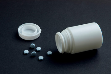 Bote de pastillas destapado con medicamento fuera y fondo negro