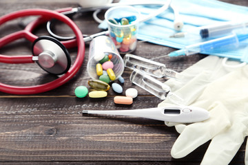Doctor's Day concept. Stethoscope with colorful pills, thermometer and pair of gloves on brown wooden table