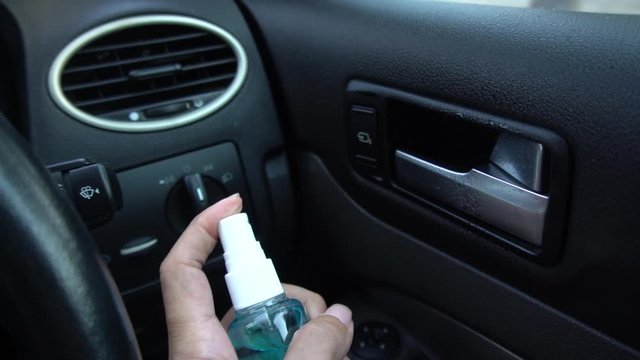 Hand of man is spraying alcohol,disinfectant spray in his car,prevent infection of Covid-19 virus,contamination of germs or bacteria,wipe clean surfaces that are frequently touched