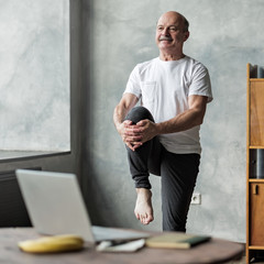 man doing yoga exercise at home using online lesson on notebook.