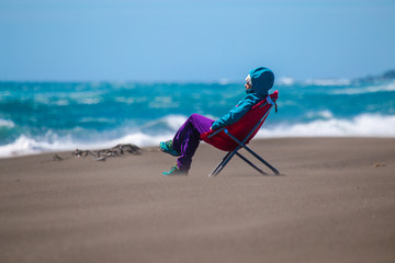 Girl photographer in a chair on the sandy shore