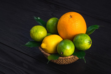 orange, lemon and three limes lie in a rustic plate on a brown table.
