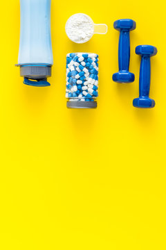 Creatine capsules, protein near shaker and dumbbells - sports supplements - flat lay on yellow background top view copy space
