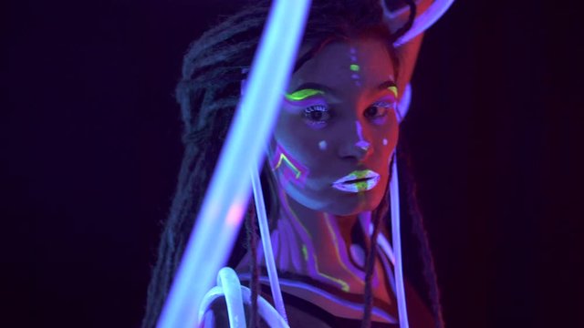 Portrait of a Girl with Dreadlocks in Neon UF Light. Model Girl dancing with glowing tubes with Psychedelic MakeUp, Art Design of Female Disco Dancer Model in UV, Colorful Abstract Make-Up.