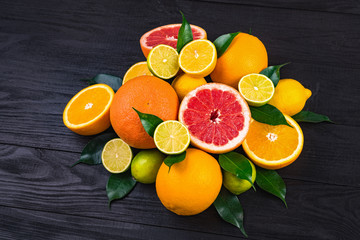 citrus fruits, half grapefruits, lemons, oranges, limes with green leaves lie on a brown wooden table