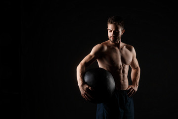 Fototapeta na wymiar a male athlete in good physical shape on a black background with a medball in his hands
