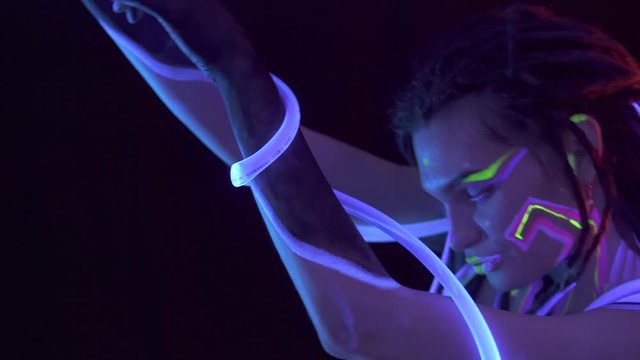 Portrait of a Girl with Dreadlocks in Neon UF Light. Model Girl dancing with glowing tubes with Psychedelic MakeUp, Art Design of Female Disco Dancer Model in UV, Colorful Abstract Make-Up.