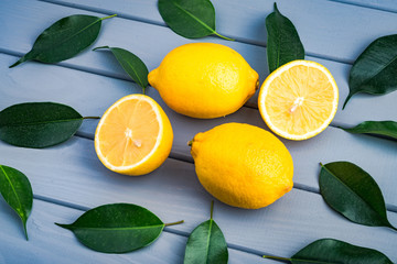 whole and sliced juicy lemons lie in a chaotic manner with blue leaves on a gray table.