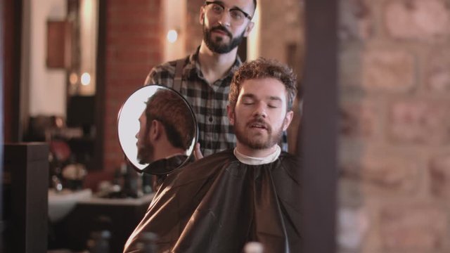 Barber in hairdresser showing client hair cut