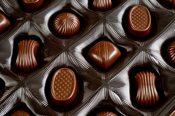 Assorted chocolates lying in a box. Background for products from chocolate and sweets. Dark chocolate.