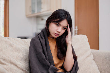 Portrait of Young woman sitting on a couch, holding her head, having a strong headache. Pandemic 2019 Coronavirus 2019-nCoV Concept.