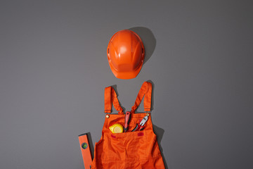 top view of orange helmet and overalls with measuring tape, screwdriver and pliers on grey...