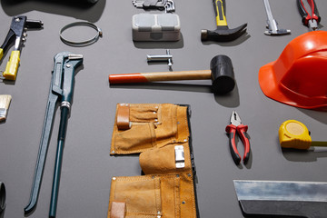 high angle view of tool belt, helmet, hammers, monkey wrench, putty knife, pliers, calipers, rivet gun and measuring tape on grey background