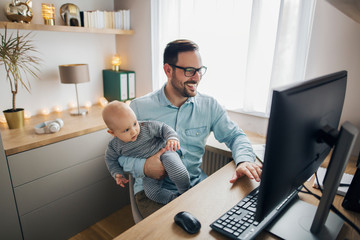 Young parent works from home and holds his baby boy.