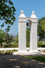 Fototapeta premium Stellenbosch, Western Cape, South Africa. Dec 2019. A slave bell mounted between two white painted pillars on a wine farm in Stellenbosch, Western cape, South Africa.
