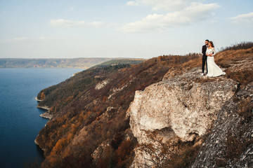 Obraz premium Beautiful bride on a mountains and river background. Cute girl in white dress. Mountains landscape and rivers in the sunset