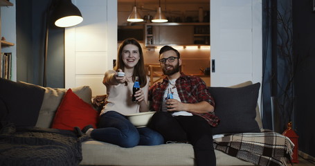 Happy beautiful young Caucasian romantic couple using TV remote control to watch movies at home...