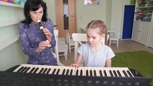 teacher teaches girl play synthesizer, plays flute