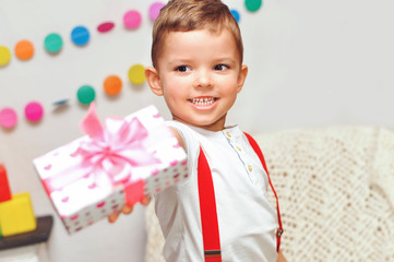 Smiling Little boy in a white T-shirt gives a gift box with a pink bow.