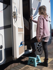 A lady motorhome owner uses a small step to enter her motorhome using the side habitation door.Vertical Image