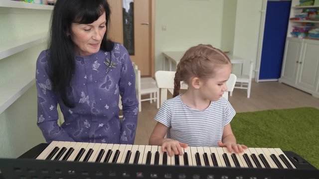 teacher teaches little girl play on synthesizer