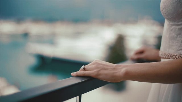 Front view of hand with precious engagement ring with huge diamond on the handrail on the open air balcony, girl dressed in white bridal attire