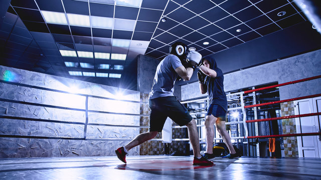 Professional boxers with gloves train fights in indoor boxing ring, dark colors - Powered by Adobe