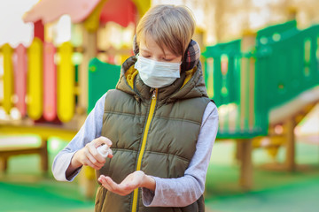 School boy wearing medical mask using sanitizer