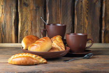 plate with fresh hot mini pies and coffee cups on wooden table, close view 