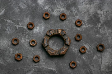 Many rusty small nuts and one large nut lie on a dark gray background with a beautiful texture. Industrial photophone.