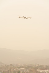 Fototapeta na wymiar 黄砂に覆われた街並みを飛ぶ飛行機
