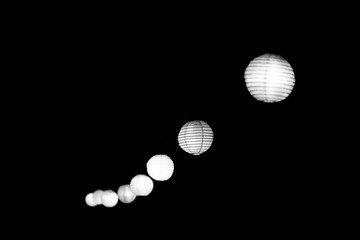 BW. A line of lanterns swinging and glowing in the dark. Photographed with selected focus and processed in black & white color.