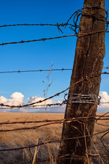 Barb wire wrapped around a weathered wood fence post on a rural ranch under a blue sky.