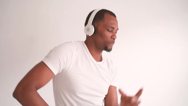 Ethnic people and music concept. Black man dancing to the rhythm and blues. Attractive african american man listening to music with bluetooth headphones. Urban style isolated on white background.