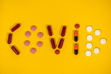Closeup top view flatlay image of word Covid 19 written on bright orange background with help of different colorful pills.