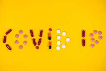 Closeup top view flatlay photography of word Covid 19 made on bright orange background with help of different colorful pills.